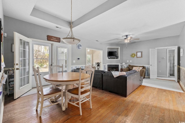 dining area with a tray ceiling, french doors, ceiling fan, and light wood-type flooring