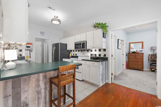 kitchen with sink, a textured ceiling, light wood-type flooring, stainless steel appliances, and white cabinets