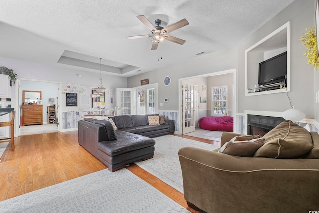 living room featuring french doors, a healthy amount of sunlight, light hardwood / wood-style floors, and a tray ceiling