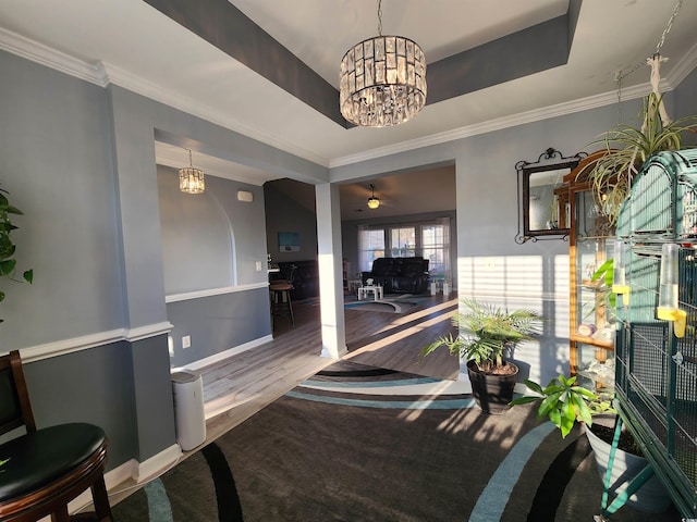 interior space featuring a raised ceiling, ornamental molding, wood-type flooring, and a notable chandelier