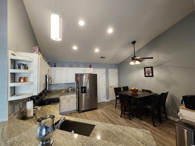 kitchen with vaulted ceiling, stainless steel fridge with ice dispenser, hanging light fixtures, light stone countertops, and white cabinets