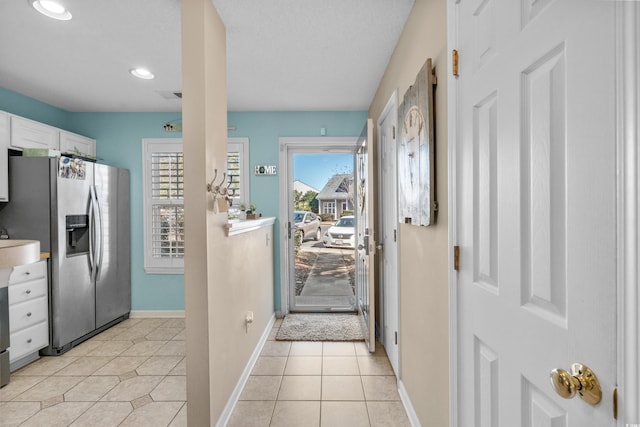 kitchen featuring visible vents, baseboards, white cabinets, light tile patterned flooring, and stainless steel fridge