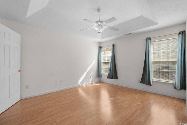 spare room with baseboards, visible vents, a raised ceiling, ceiling fan, and wood finished floors