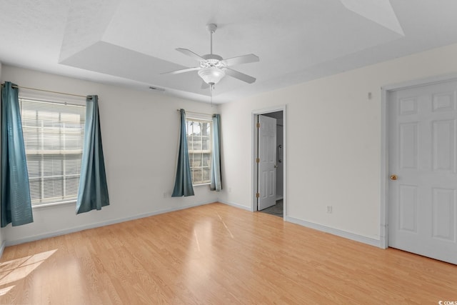 unfurnished bedroom with a raised ceiling, multiple windows, and wood finished floors