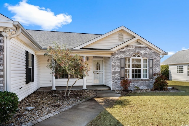 view of front of property with covered porch, brick siding, a front lawn, and a shingled roof