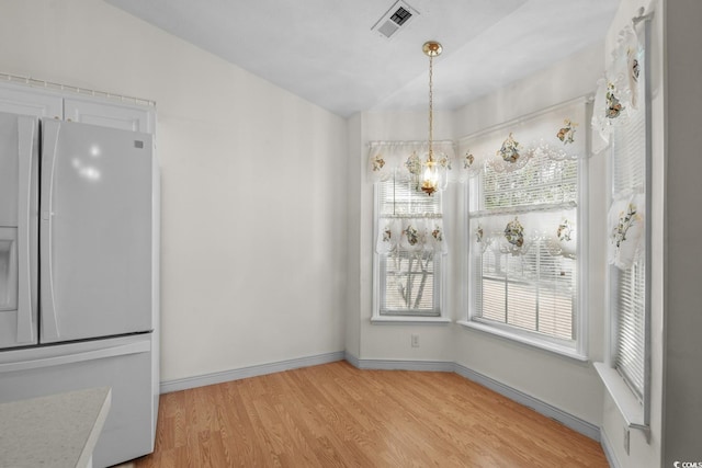 unfurnished dining area featuring light wood-type flooring, a healthy amount of sunlight, baseboards, and visible vents