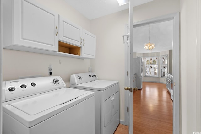 clothes washing area with baseboards, light wood-type flooring, independent washer and dryer, cabinet space, and an inviting chandelier