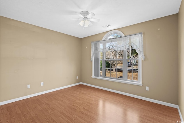 empty room featuring a ceiling fan, visible vents, baseboards, and wood finished floors