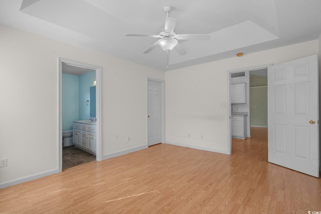 unfurnished bedroom with baseboards, a raised ceiling, light wood-style flooring, ensuite bathroom, and a sink