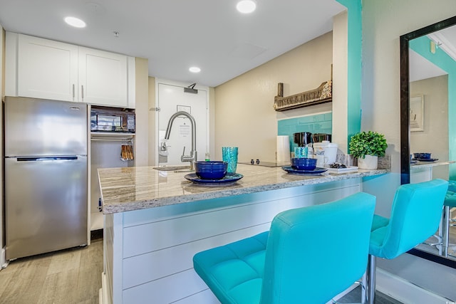 kitchen featuring sink, light stone counters, stainless steel refrigerator, and kitchen peninsula