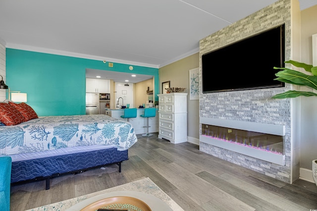 bedroom featuring sink, crown molding, stainless steel refrigerator, a large fireplace, and light wood-type flooring