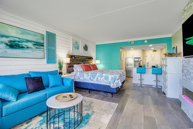 bedroom with hardwood / wood-style floors, crown molding, and stainless steel refrigerator