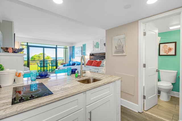 kitchen featuring sink, light wood-type flooring, black electric cooktop, light stone countertops, and white cabinets