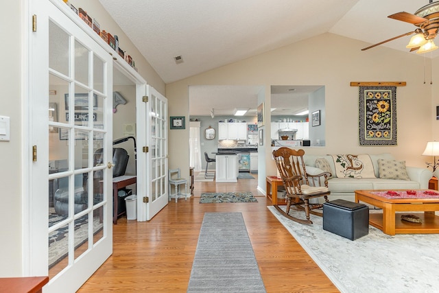 living room with lofted ceiling, french doors, and light wood-type flooring