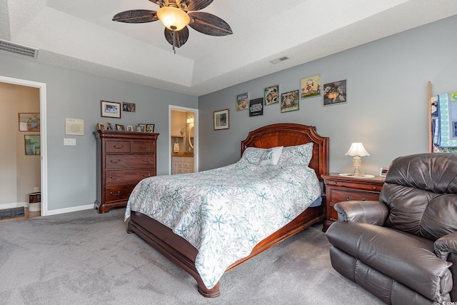 bedroom with ceiling fan, ensuite bathroom, a textured ceiling, light colored carpet, and a raised ceiling