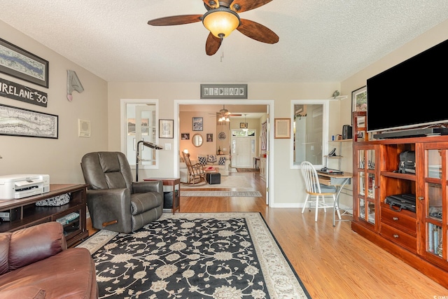 living room featuring ceiling fan, a textured ceiling, and light wood-type flooring