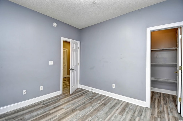 unfurnished bedroom featuring hardwood / wood-style floors, a walk in closet, a closet, and a textured ceiling