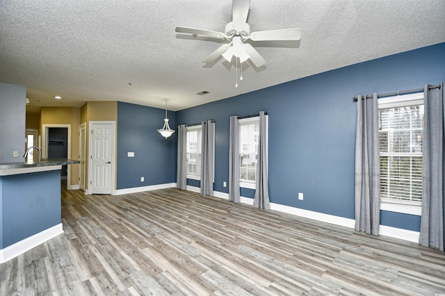 unfurnished living room featuring ceiling fan, a textured ceiling, a healthy amount of sunlight, and light wood-type flooring