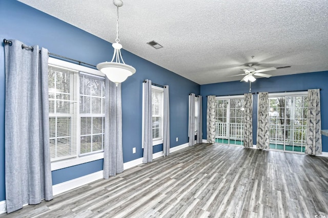 unfurnished dining area with ceiling fan, wood-type flooring, and a textured ceiling