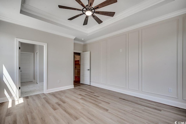 interior space with baseboards, ornamental molding, light wood-style floors, and a raised ceiling