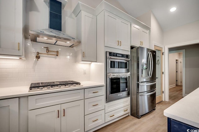 kitchen with wall chimney exhaust hood, stainless steel appliances, light countertops, and decorative backsplash