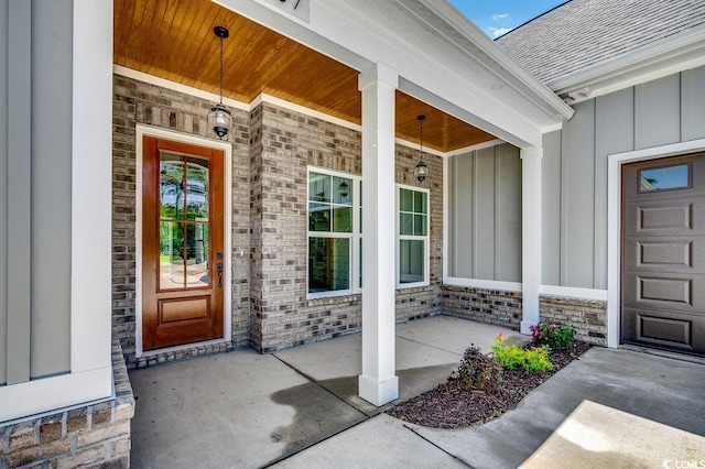 doorway to property with board and batten siding, brick siding, covered porch, and roof with shingles