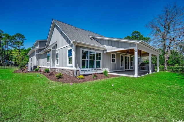 back of property with board and batten siding, a ceiling fan, a yard, and a patio
