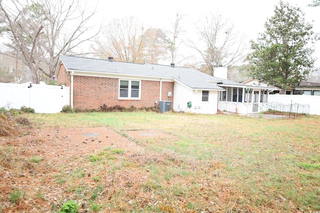 rear view of house with central AC, a sunroom, and a lawn