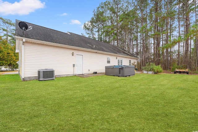 rear view of house featuring a hot tub, a yard, and central air condition unit