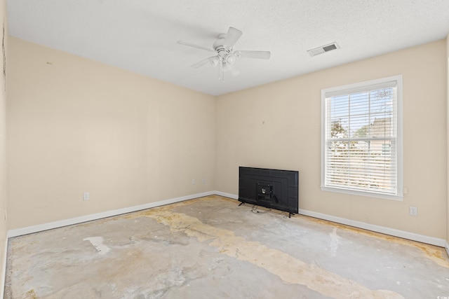 empty room featuring ceiling fan, a textured ceiling, concrete floors, and a wood stove