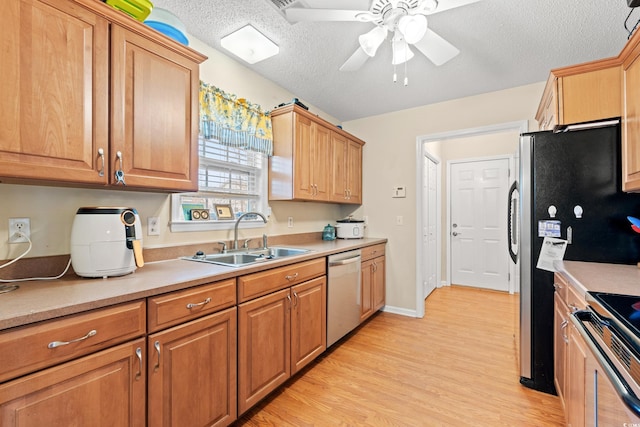 kitchen with sink, a textured ceiling, ceiling fan, stainless steel appliances, and light hardwood / wood-style floors