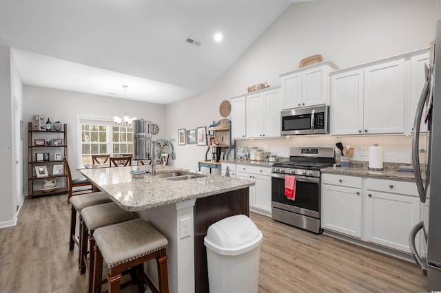 kitchen with appliances with stainless steel finishes, sink, white cabinets, hanging light fixtures, and a kitchen island with sink