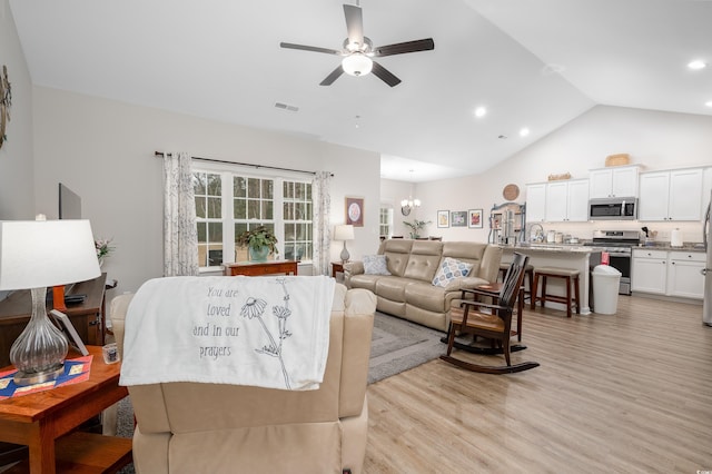 living room featuring lofted ceiling, ceiling fan with notable chandelier, and light hardwood / wood-style floors