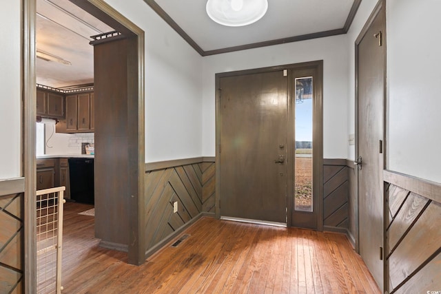 entryway with a wainscoted wall, wood finished floors, visible vents, and crown molding