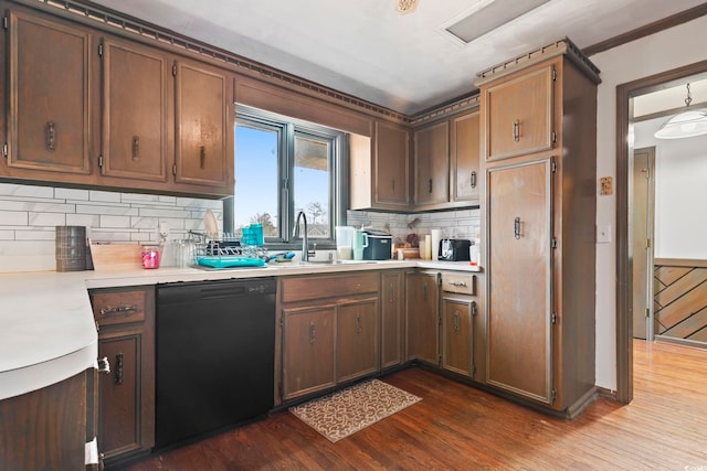 kitchen with a sink, black dishwasher, light countertops, decorative backsplash, and dark wood finished floors