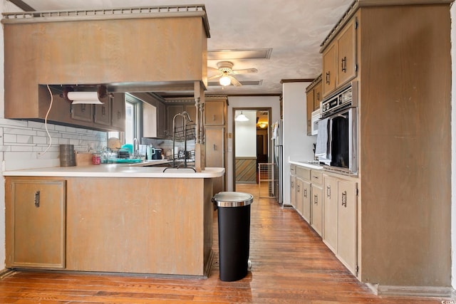 kitchen with oven, a peninsula, light countertops, crown molding, and light wood-type flooring