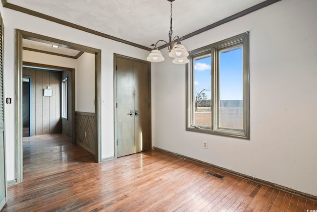 spare room featuring a chandelier, wood finished floors, visible vents, baseboards, and ornamental molding