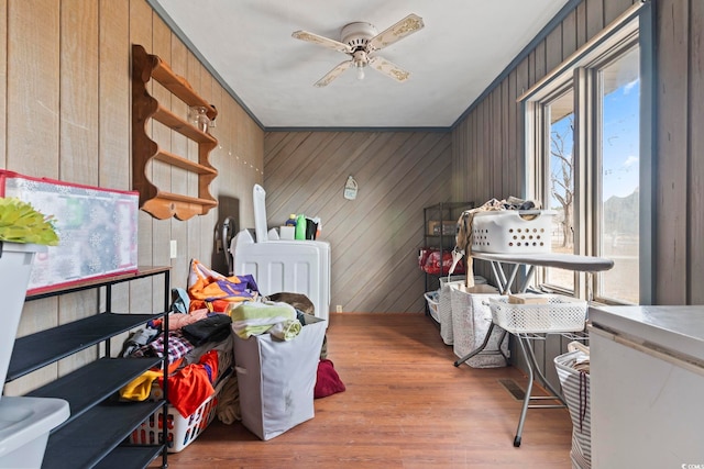 interior space featuring light wood-type flooring, wood walls, ceiling fan, and washer / clothes dryer