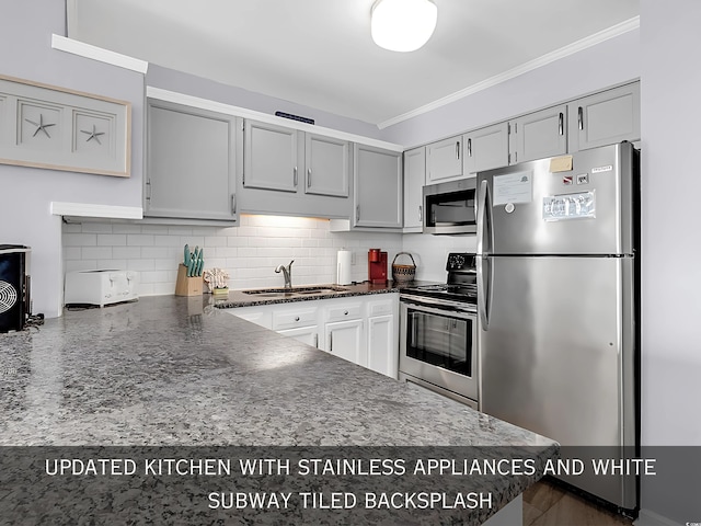 kitchen with dark stone countertops, a sink, stainless steel appliances, crown molding, and tasteful backsplash