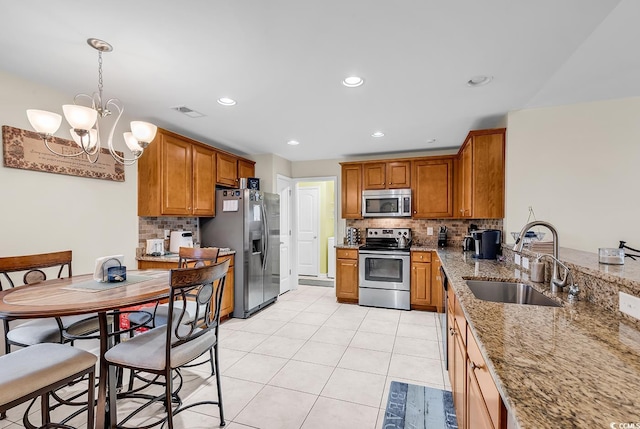 kitchen with sink, light stone counters, tasteful backsplash, decorative light fixtures, and stainless steel appliances