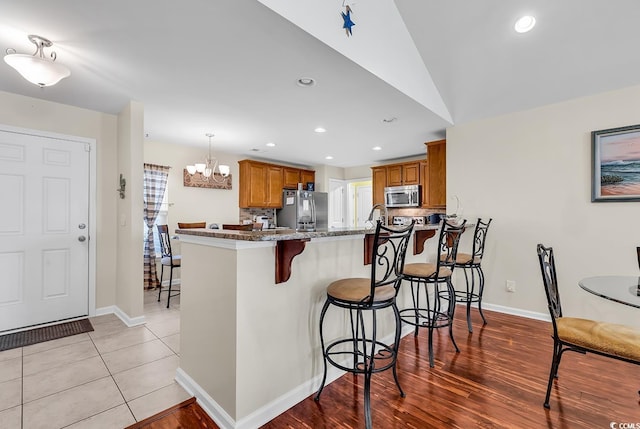 kitchen featuring an inviting chandelier, stainless steel appliances, light stone counters, a kitchen bar, and kitchen peninsula