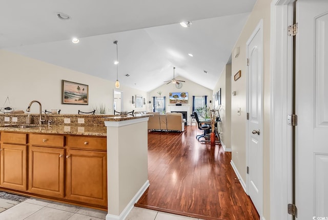 kitchen featuring lofted ceiling, sink, ceiling fan, light stone countertops, and light hardwood / wood-style floors