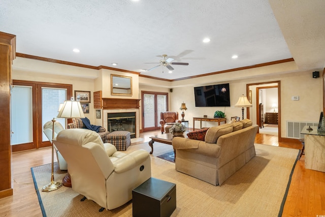 living room with crown molding, light hardwood / wood-style flooring, a tile fireplace, and a textured ceiling