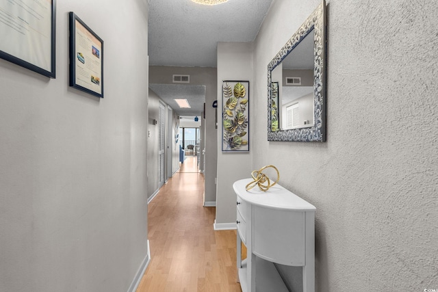 hall with a textured ceiling and light hardwood / wood-style flooring