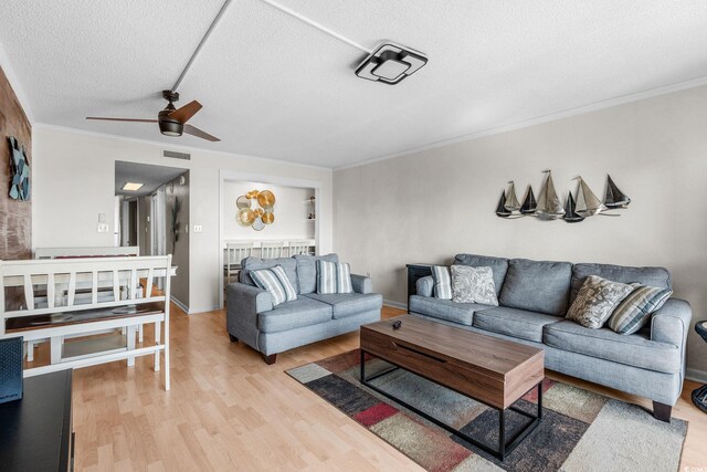 living room featuring crown molding, ceiling fan, light hardwood / wood-style floors, and a textured ceiling