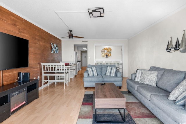 living room with crown molding, wood walls, ceiling fan, and light hardwood / wood-style flooring