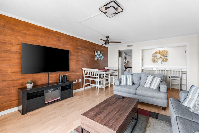 living room with light hardwood / wood-style flooring, ornamental molding, ceiling fan, and wood walls