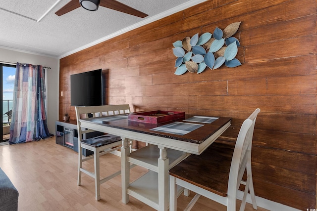 dining area featuring wood walls, wood-type flooring, a textured ceiling, ornamental molding, and ceiling fan