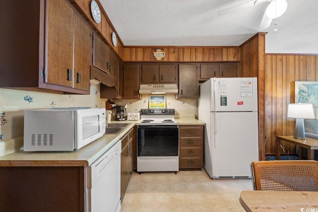 kitchen featuring sink, white appliances, ceiling fan, a textured ceiling, and wood walls