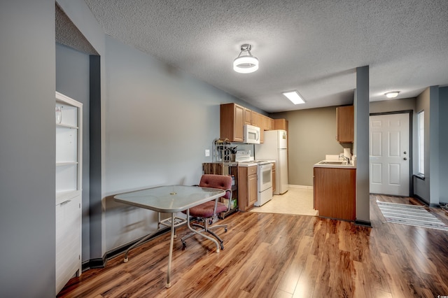 kitchen with sink, white appliances, a textured ceiling, and light wood-type flooring